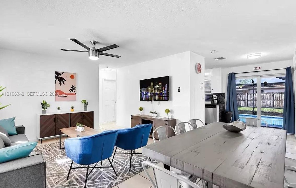 Open-concept main living area featuring neutral wall paint, tile flooring, a multi-blade ceiling fan, and sliding glass doors providing outdoor access