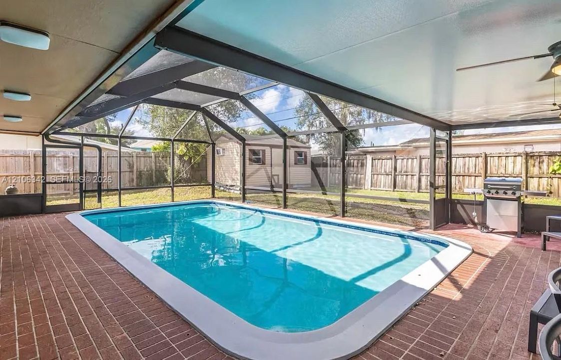Screened lanai featuring a swimming pool, covered patio area, brick pavers, and wood privacy fencing