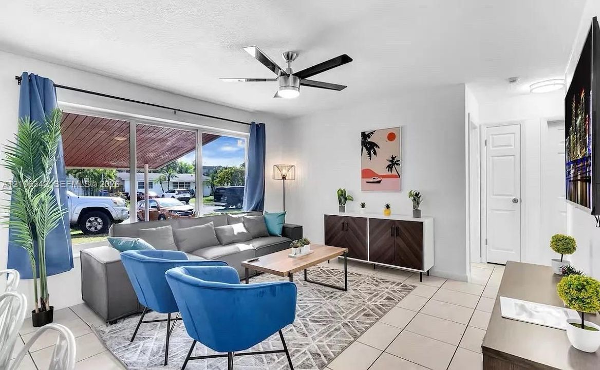 Large picture window with metal frame, light-colored tile flooring, brushed-nickel ceiling fan with integrated lighting, and multi-panel interior doors