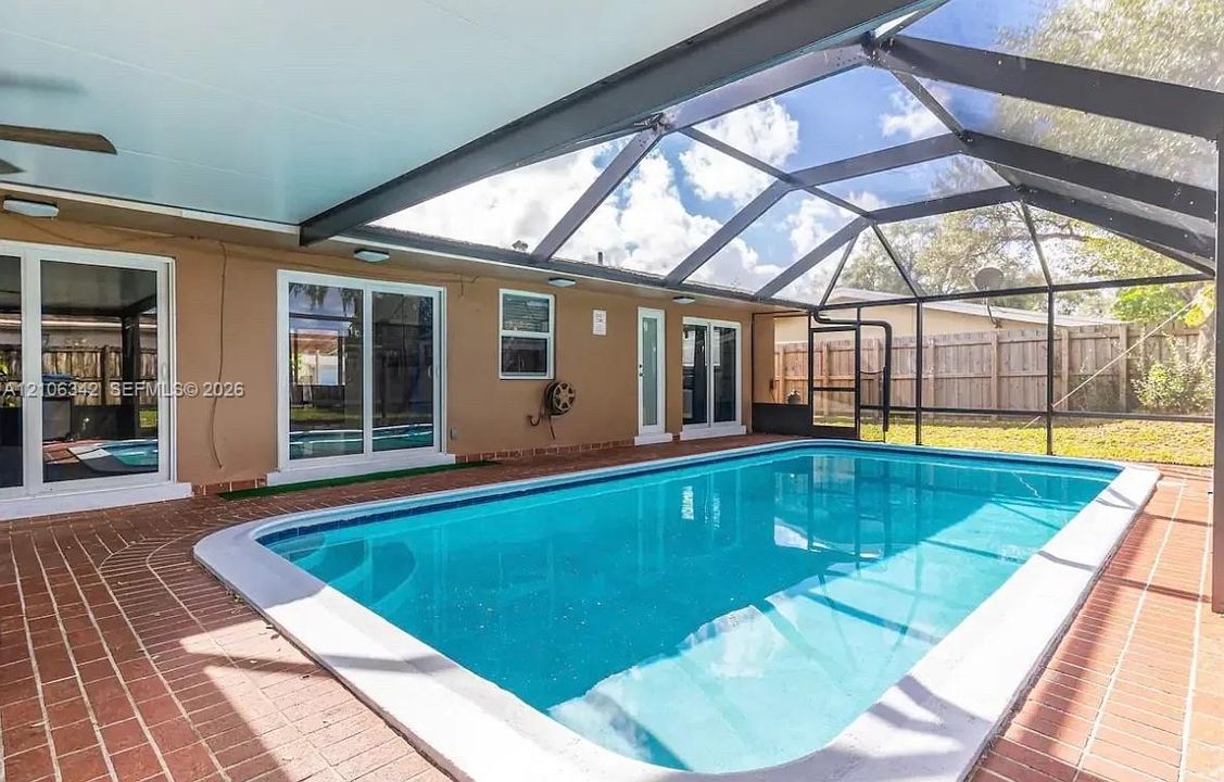Screen-enclosed swimming pool featuring a brick-paved patio, covered lanai, and multiple sliding glass door entries