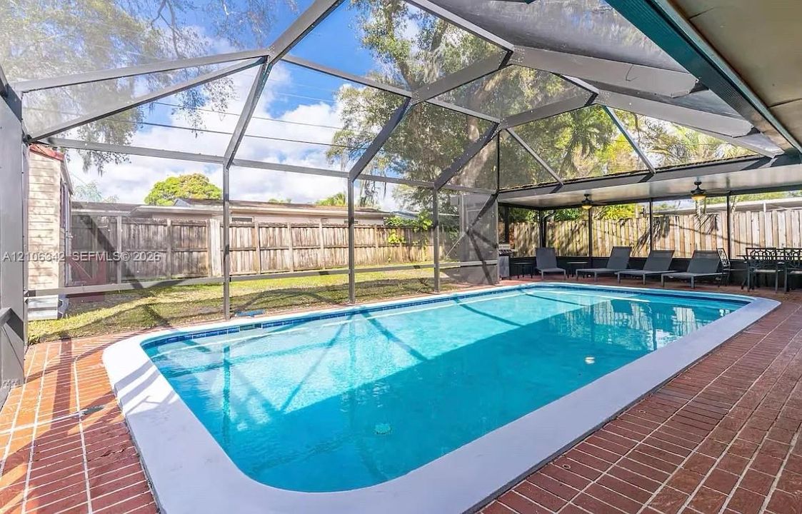 Screen-enclosed swimming pool featuring a brick-paved patio, covered lanai, and wood-panel perimeter fencing
