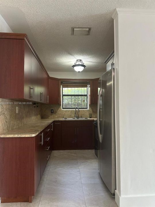 Kitchen featuring dark wood-finish cabinetry, stone-patterned countertops, a stainless steel refrigerator, tile flooring, and a single-basin sink with a gooseneck faucet