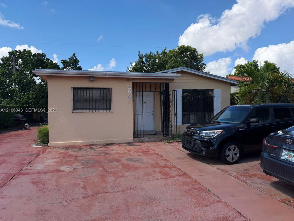 Single-story residence featuring a painted masonry exterior, metal security bars on windows, a covered recessed entryway with security gate, and a paved driveway