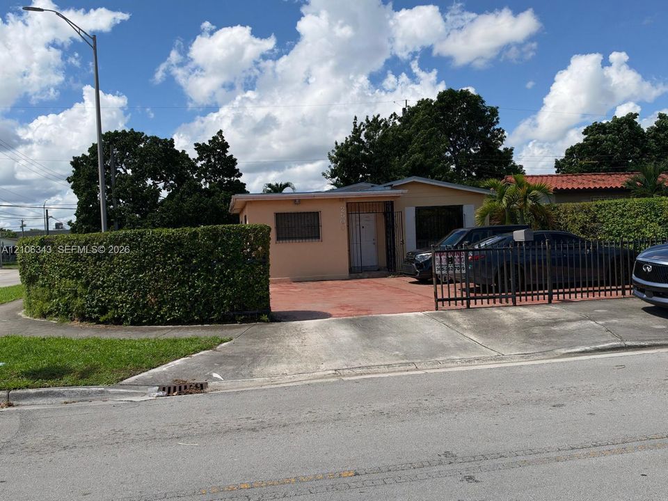 Single-story exterior featuring a concrete driveway, metal perimeter fencing, and mature hedge landscaping
