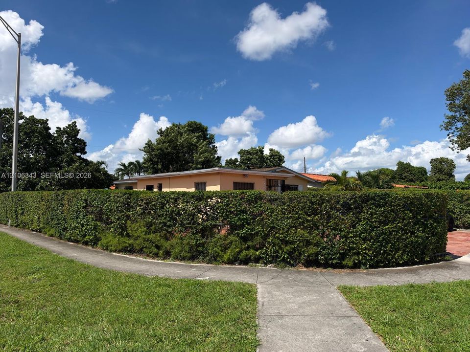 Single-story residence featuring a perimeter of mature hedge landscaping and a concrete sidewalk