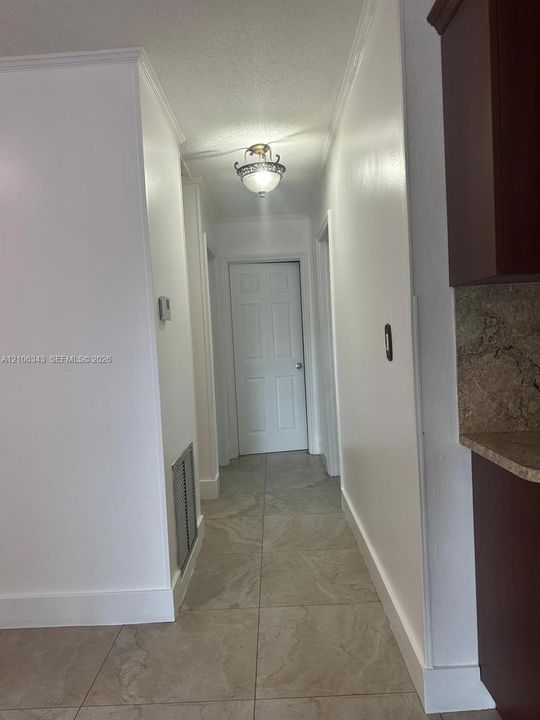 Hallway featuring neutral-toned tile flooring, semi-flush mount ceiling lighting, and six-panel interior doors