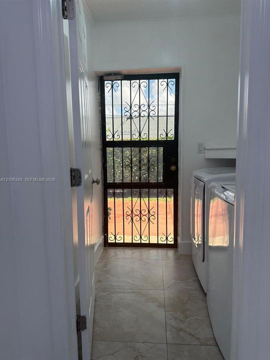 Laundry space featuring neutral tile flooring, built-in shelving, and a metal security screen door