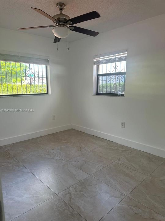 Neutral-toned tile flooring, ceiling fan with integrated lighting, and metal security bars on exterior windows