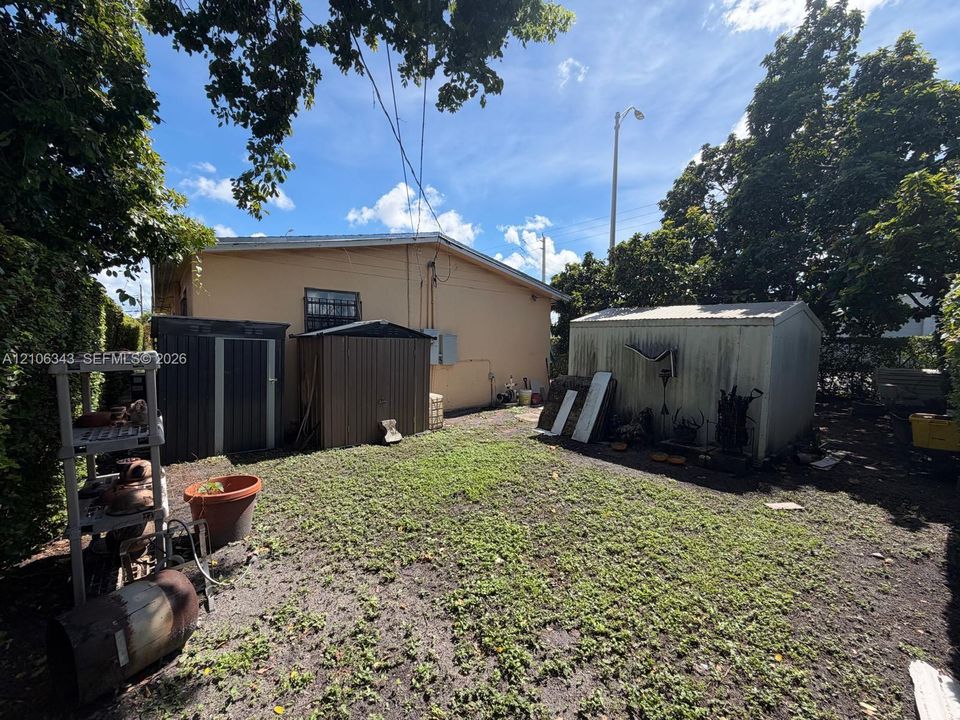 Backyard space featuring two metal storage structures, exterior wall siding, and mature trees