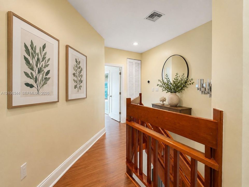 Hallway featuring wood-finish flooring, a wood balustrade staircase railing, and a circular wall-mounted mirror