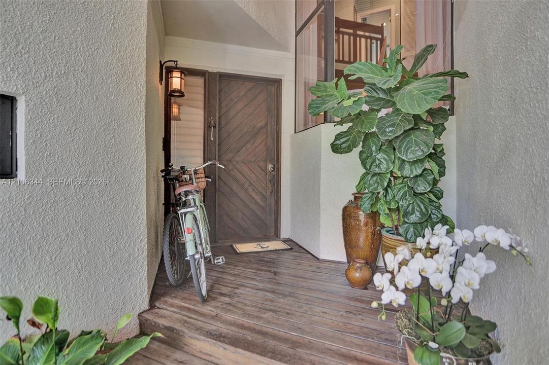 Covered entryway featuring a wood-finish plank floor, a diagonal-patterned wood entry door, and an integrated exterior lantern-style wall sconce