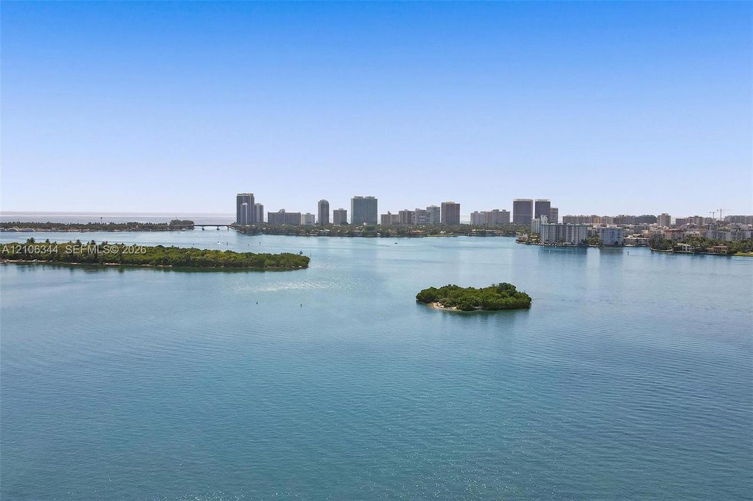 Expansive coastal water frontage with small mangrove islands and a distant city skyline