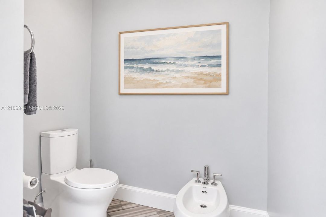 White porcelain toilet, bidet with chrome hardware, and metallic circular towel ring