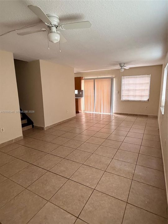 Open-concept interior featuring large-format ceramic tile flooring, dual ceiling fans, sliding glass doors, and recessed window treatments