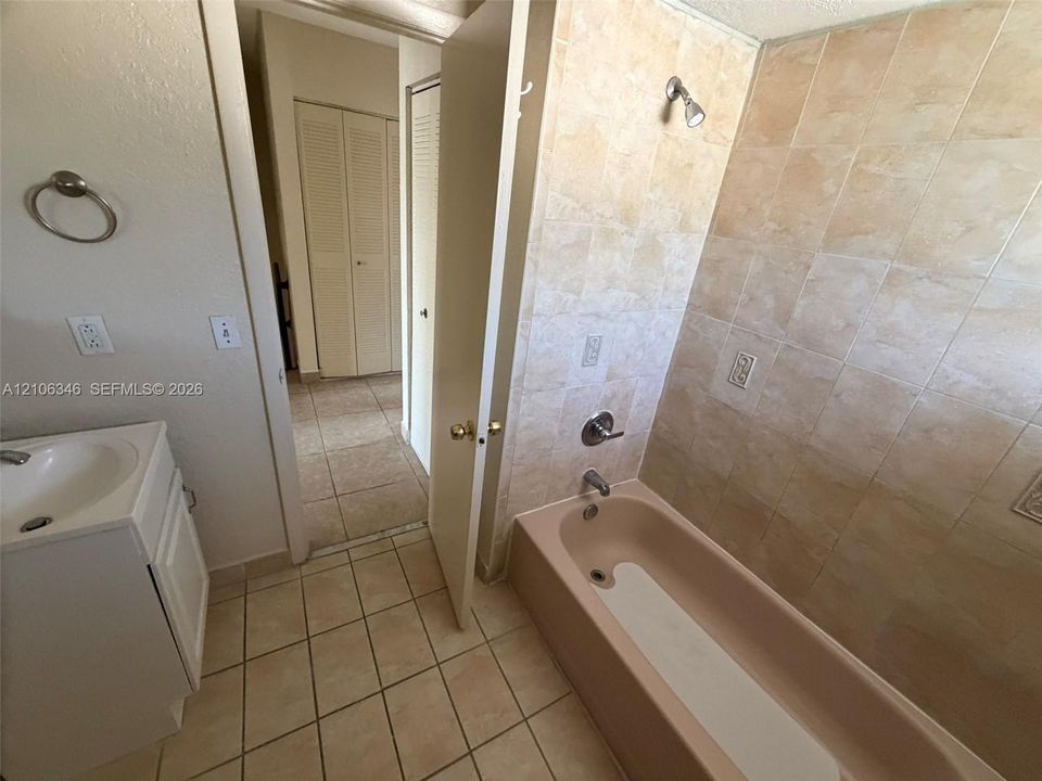 Bathroom featuring ceramic tile flooring, built-in vanity with integrated basin, tub and shower combination, and neutral ceramic wall tile surround