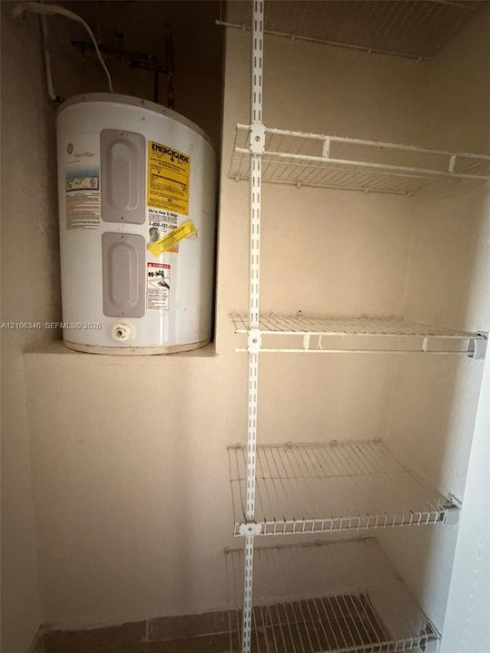 Utility area featuring a mounted water heater and adjustable wire shelving system