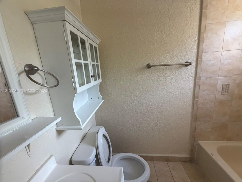 Bathroom featuring a wall-mounted white cabinet with glass-panel doors, tiled shower enclosure, brushed nickel towel ring, and brushed nickel towel bar