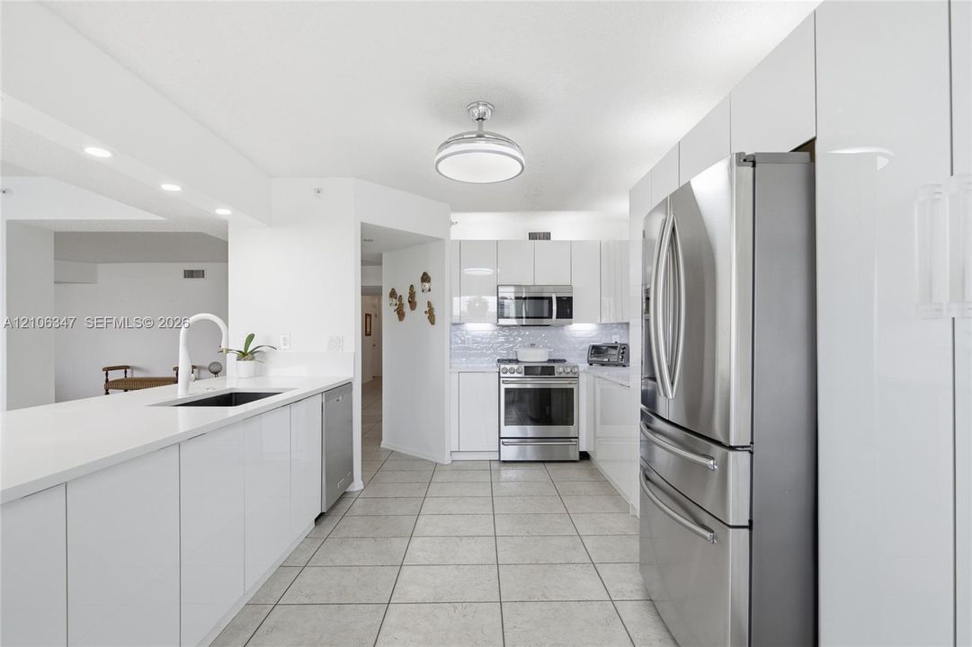Kitchen featuring glossy white flat-panel cabinetry, stainless steel appliances, white stone countertops, tile flooring, and a modern gooseneck faucet