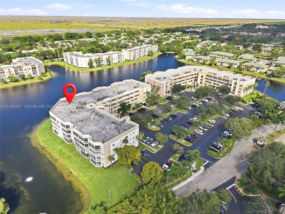 Multi-story residential building situated on a waterfront lot featuring surface parking and mature landscaping