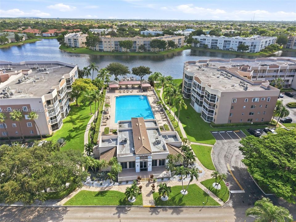 Community pool area featuring a paved deck, pergola, and direct water frontage with manicured landscaping and mature palm trees