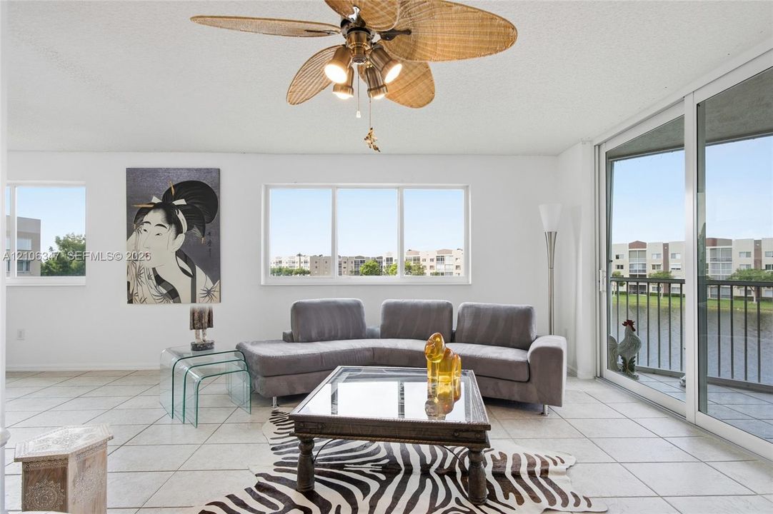 Living area featuring large format tile flooring, a multi-blade ceiling fan with integrated lighting, oversized picture windows, and sliding glass doors with direct exterior access