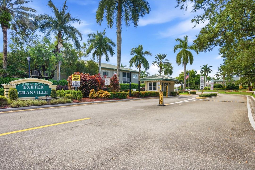 Gated community entrance featuring a monitored guardhouse, custom signage, mature palm trees, and professional landscaping