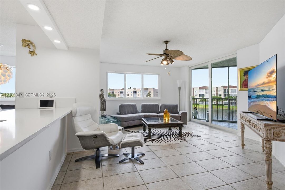 Living area featuring neutral tile flooring, recessed lighting, a ceiling fan with integrated lighting, and sliding glass doors leading to a balcony