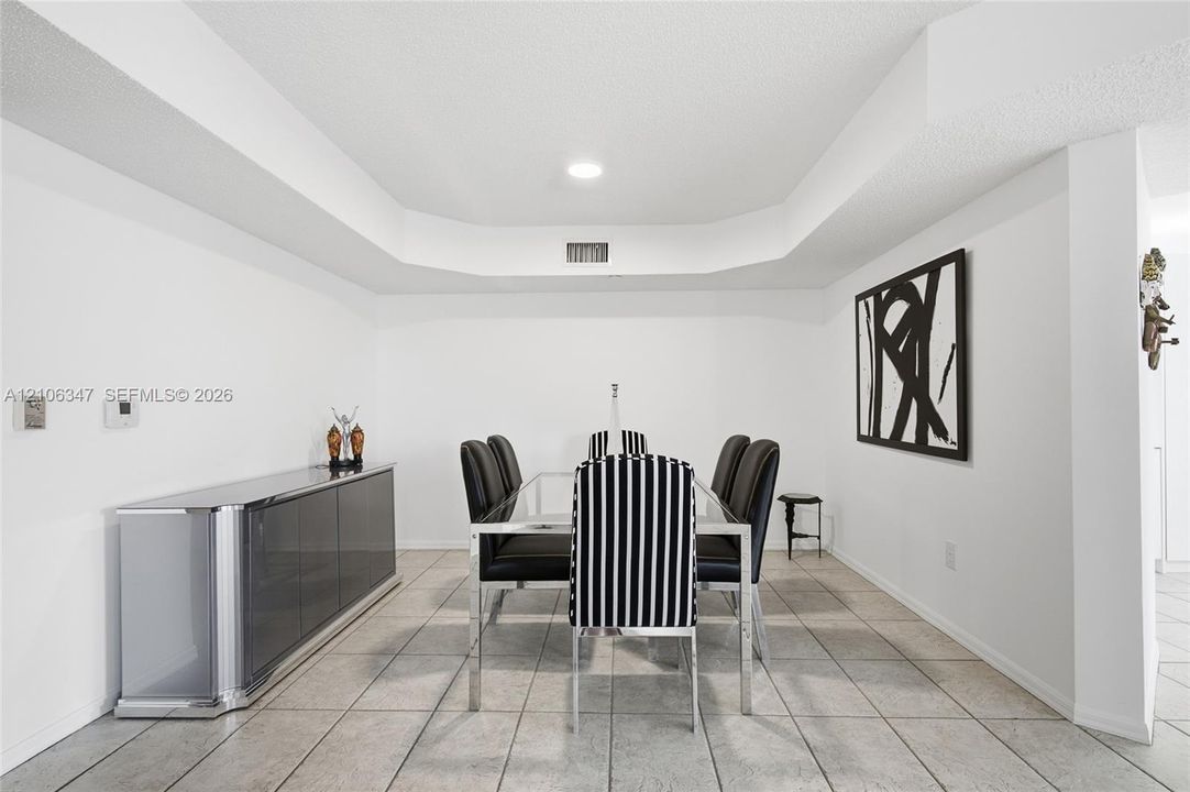 Dining area featuring tile flooring, recessed ceiling lighting, and a tiered tray ceiling design