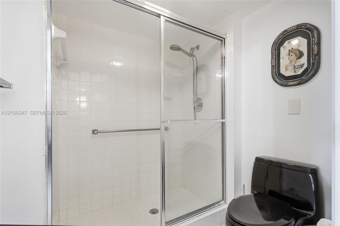 Walk-in shower enclosure with white tiled surround, chrome sliding doors, wall-mounted adjustable shower head, and integrated grab bar