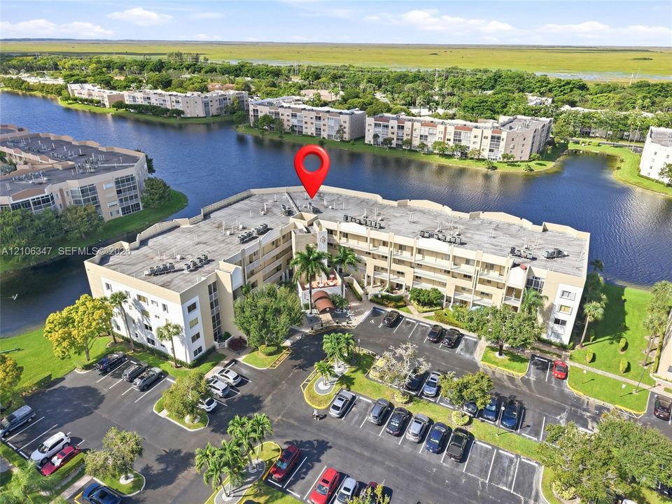 Aerial perspective featuring multi-story residential buildings, water frontage, landscaped grounds with mature palm trees, and dedicated asphalt parking