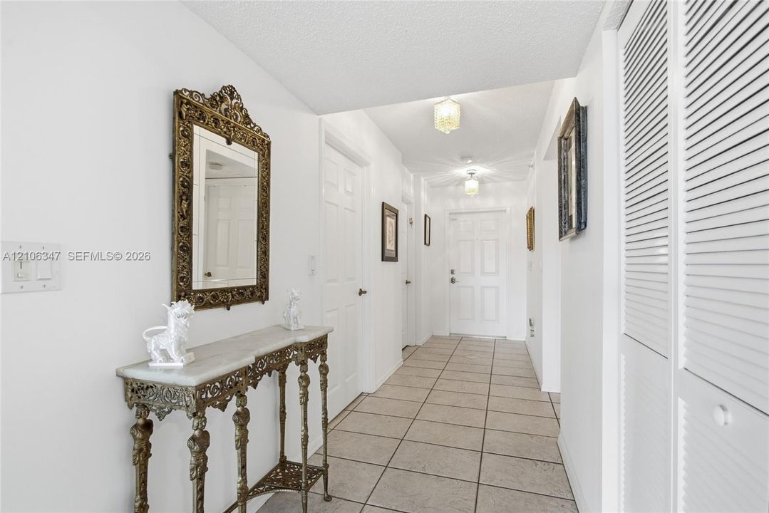 Entryway featuring neutral tile flooring, multi-panel doors, ceiling-mounted light fixtures, and white louvered closet doors