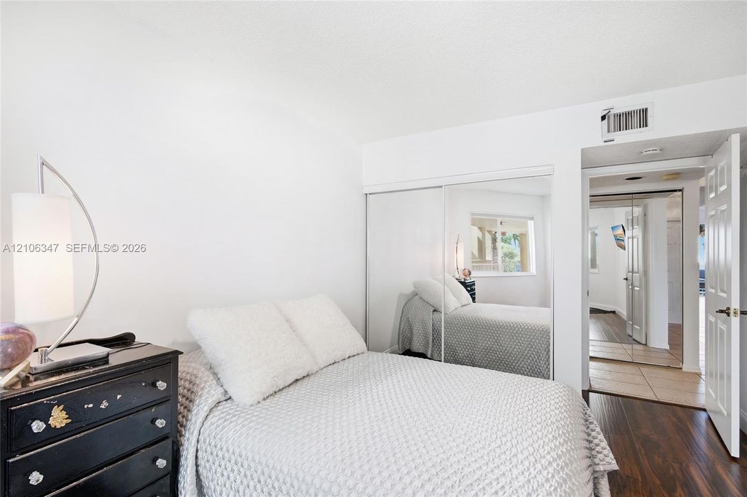 Room featuring wood-finish flooring, sliding mirror-panel closet doors, and a six-panel interior door