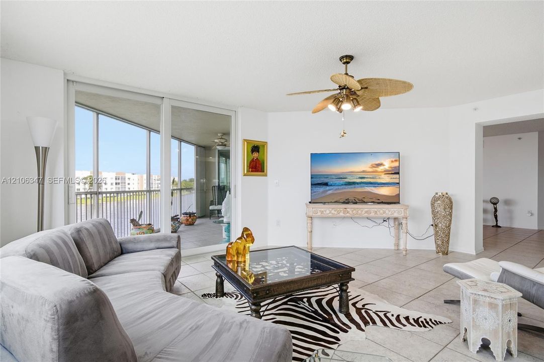 Living area featuring large-format ceramic tile flooring, floor-to-ceiling sliding glass doors, and a ceiling fan with integrated lighting