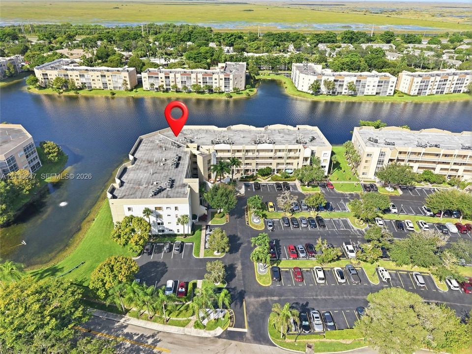 Aerial perspective of a multi-story residential building featuring waterfront positioning, dedicated surface parking, and manicured landscaping