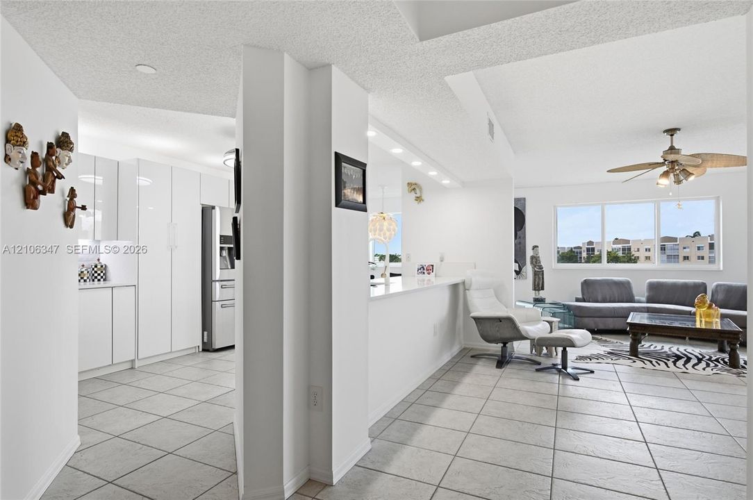 Kitchen featuring high-gloss white cabinetry, stone-finish countertops, tile flooring, and integrated lighting, including a multi-light ceiling fan