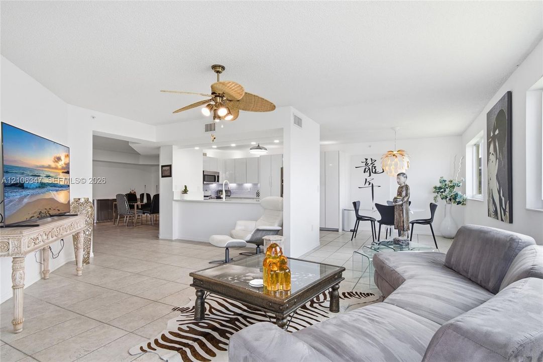 Open-concept interior featuring large-format ceramic tile flooring, a kitchen breakfast bar, and a ceiling fan with woven-style blades