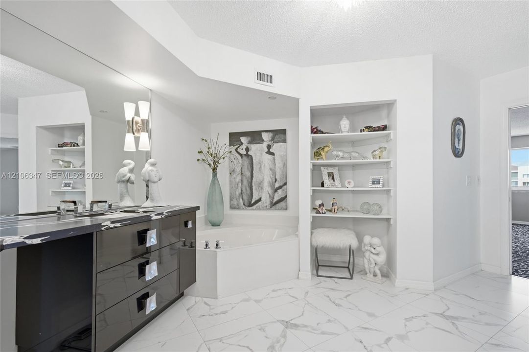 Bathroom featuring large-format tile flooring, a deep soaking tub, high-gloss cabinetry, a sprawling wall mirror, and built-in corner shelving