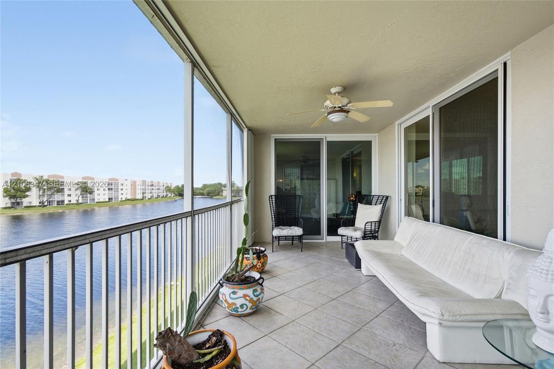 Screened-in balcony featuring tile flooring, a ceiling fan, and metal railings overlooking a lake