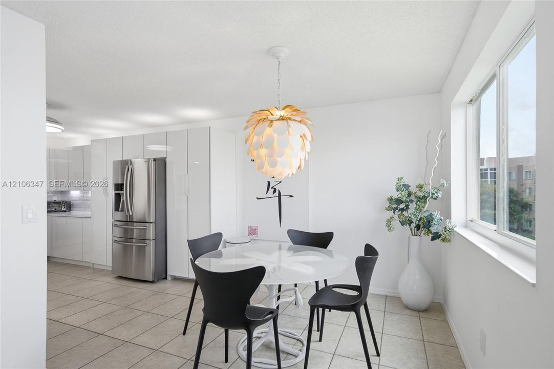 Modern kitchen featuring high-gloss white cabinetry, stainless steel refrigerator, tile flooring, and a decorative pendant light fixture