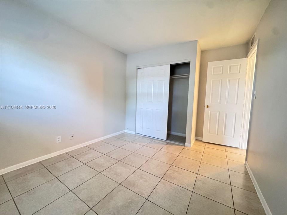 Neutral-toned room featuring large-format ceramic tile flooring, a six-panel interior door, and a built-in closet with sliding doors