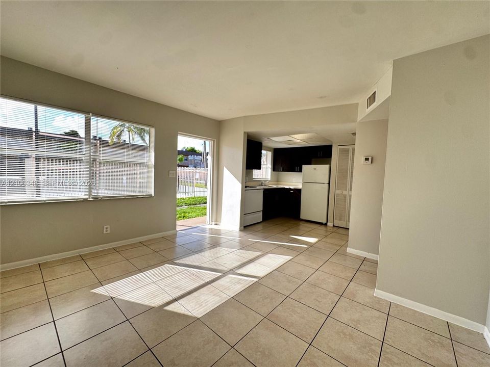 Open-concept interior featuring large-format tile flooring, oversized windows, and a kitchen equipped with dark cabinetry, white appliances, and a closet with louvered doors