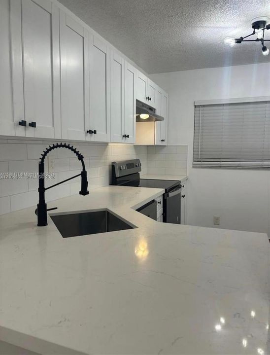 Kitchen featuring white shaker-style cabinetry, white countertops, a subway tile backsplash, a matte black gooseneck faucet, and a multi-bulb light fixture