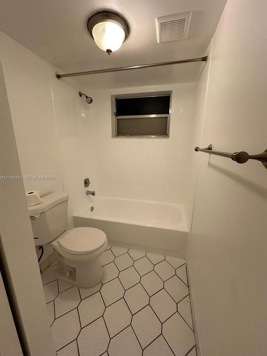 Bathroom featuring a white porcelain tub with integrated shower surround, hexagonal floor tile, chrome-finished hardware, and a semi-flush mount ceiling fixture