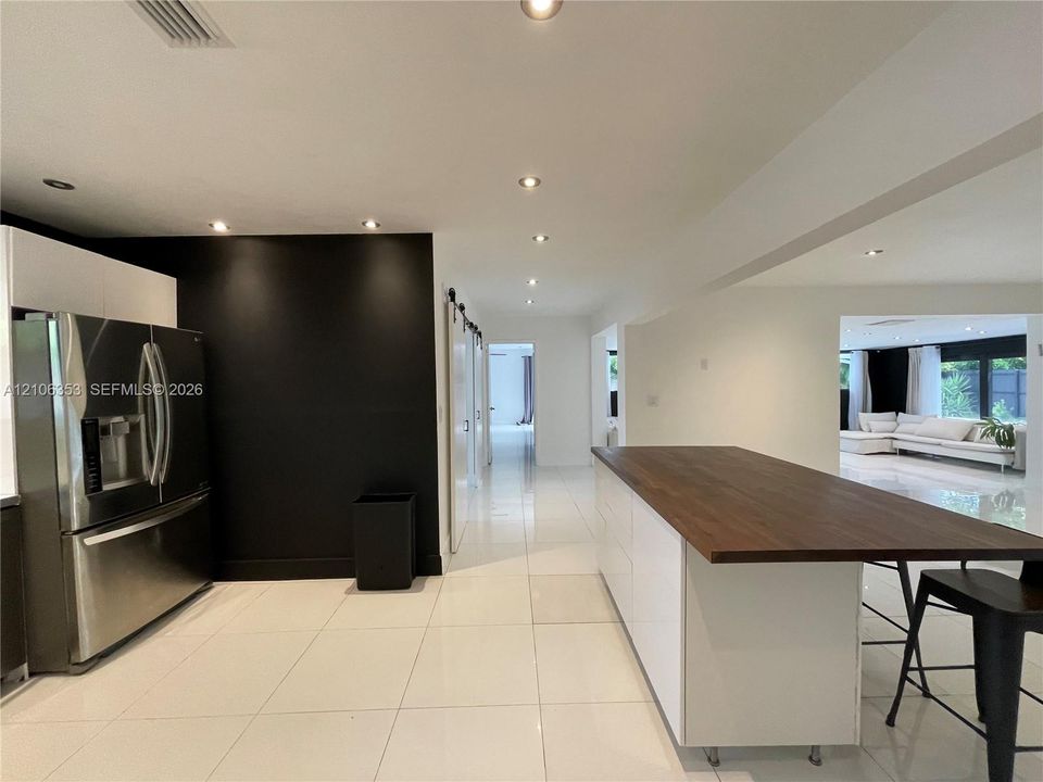 Kitchen featuring a white cabinetry island with a wood-finish countertop, high-gloss large-format tile flooring, stainless steel refrigerator, and recessed lighting