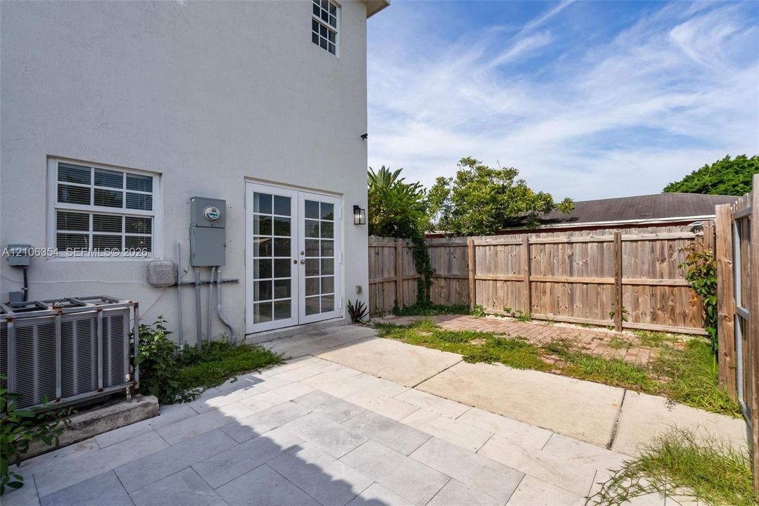 Exterior patio area featuring large-format stone pavers, white French doors, and a wood privacy fence