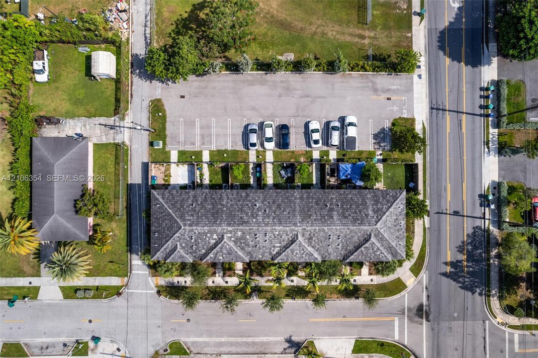 Aerial perspective featuring a multi-unit residential building with a hipped roof, dedicated surface parking lot, paved walkways, and mature landscaping