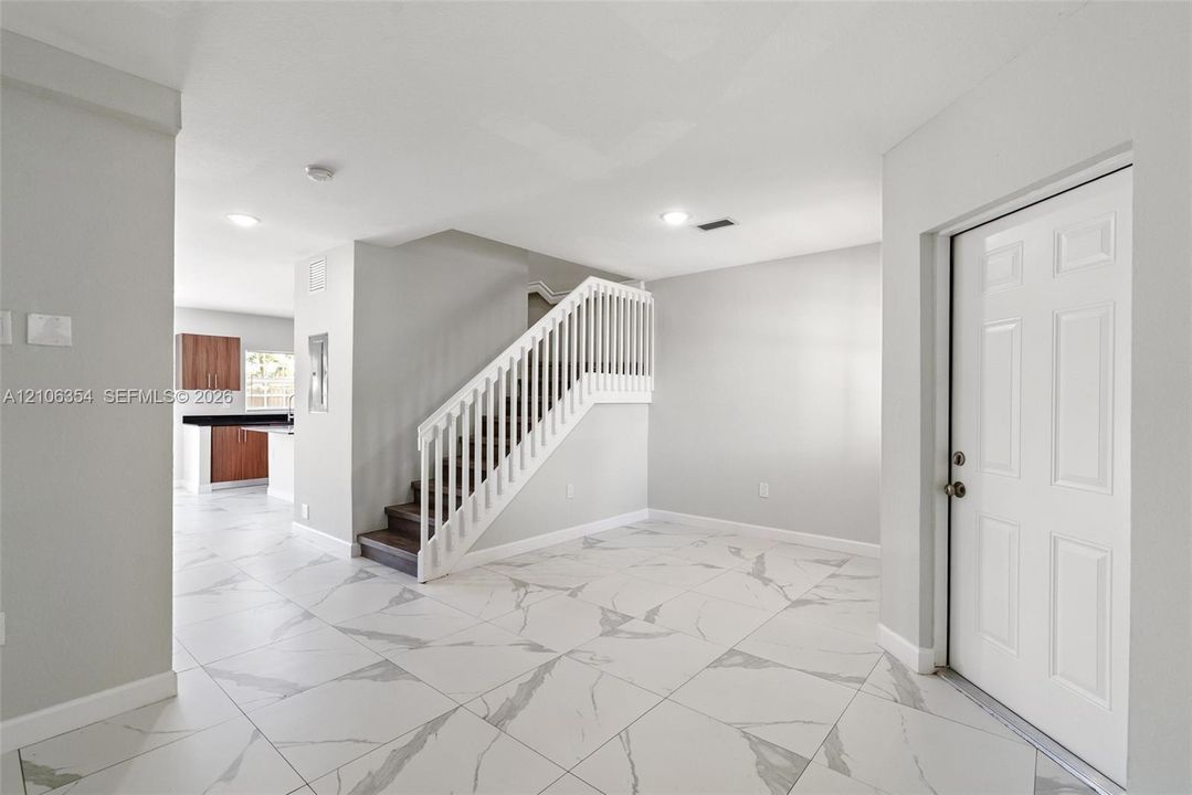 Entryway featuring large-format veined tile flooring, a staircase with a white balustrade and wood-finish treads, recessed lighting, and a six-panel entry door