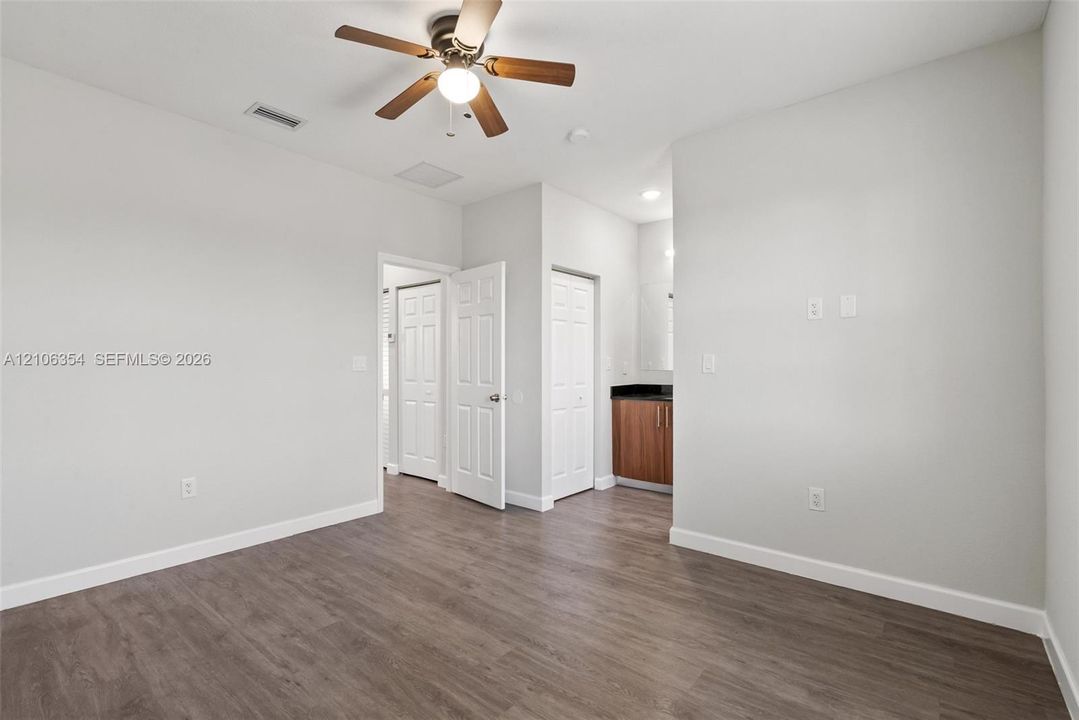 Neutral-toned interior space featuring wood-finish flooring, a ceiling fan with integrated lighting, and multiple paneled doors