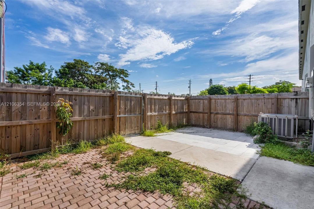 Enclosed backyard featuring a wood privacy fence, a brick paver patio, a concrete slab, and an exterior HVAC unit