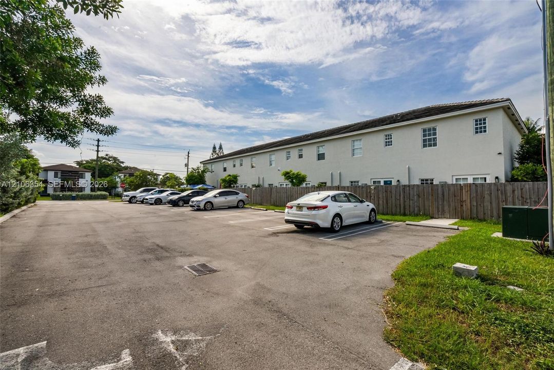Asphalt parking lot featuring painted stall markings, wood privacy fencing, and exterior lighting fixtures